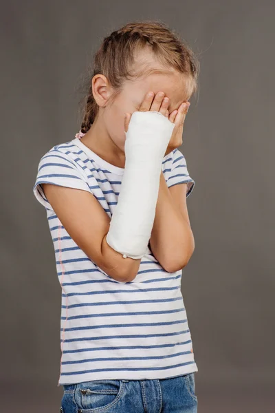 Smutna dziewczyna ze złamaną rękę stoi na szarym tle. Med — Zdjęcie stockowe