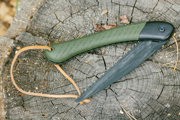 Folding saw lying on a wooden stump — Zdjęcie stockowe