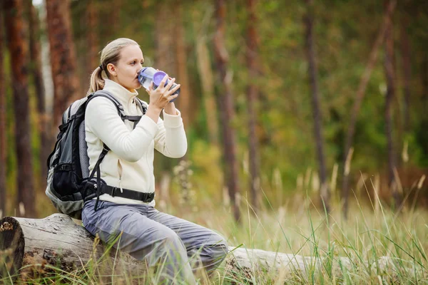 Mujer joven bebiendo agua con mochila en el valle del bosque — Foto de Stock