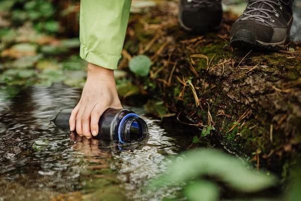 Mulher tomando água da primavera da floresta em viagem de caminhada — Fotografia de Stock