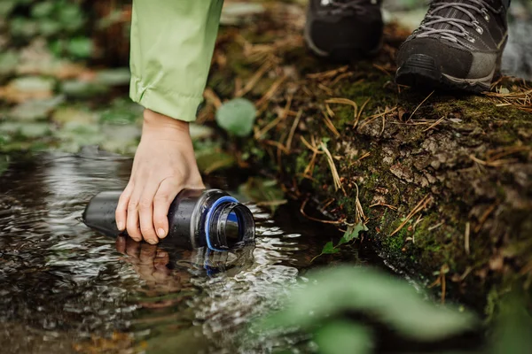 Frau entnimmt auf Wandertour Wasser aus Waldquelle — Stockfoto