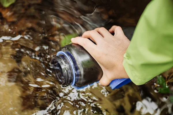 Frau entnimmt auf Wandertour Wasser aus Waldquelle — Stockfoto