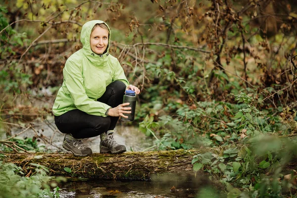 Frau entnimmt auf Wandertour Wasser aus Waldquelle — Stockfoto