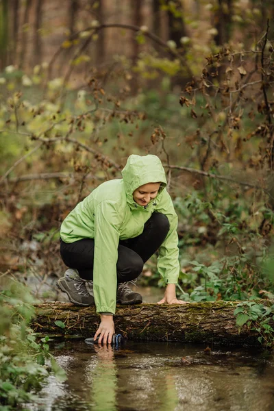Жінка бере воду з лісової весни під час походу — стокове фото