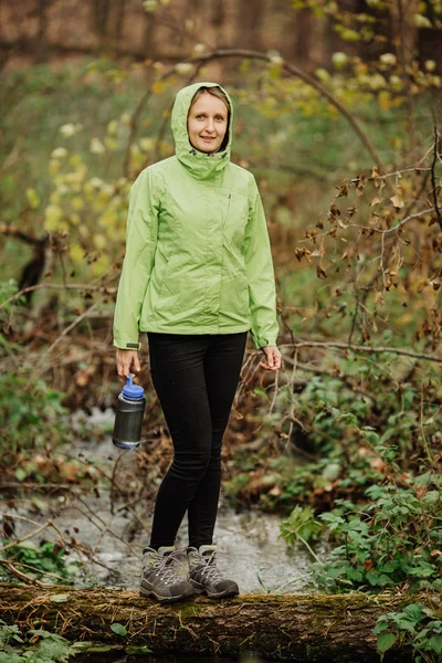 Frau entnimmt auf Wandertour Wasser aus Waldquelle — Stockfoto