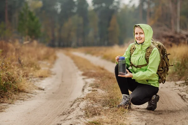 Mujer joven bebiendo agua con mochila en el valle del bosque — Foto de Stock