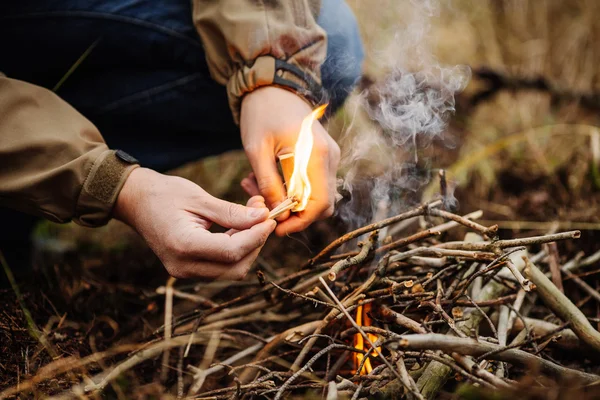 Молодой человек разжигает огонь в летнем лесу — стоковое фото