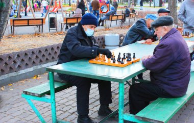 Maskeli yaşlı adamlar, parkta satranç oynuyorlar.