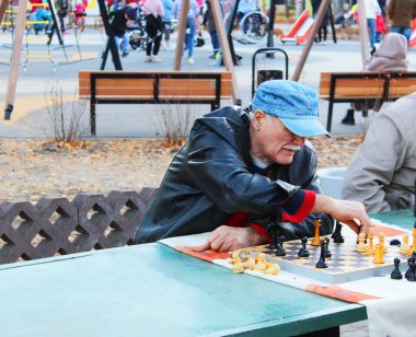 Maskeli yaşlı adamlar, parkta satranç oynuyorlar.