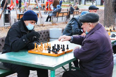 Maskeli yaşlı adamlar, parkta satranç oynuyorlar.