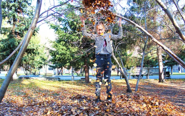 Meisje dat speelt met herfstbladeren. verstrooit bladeren in het park en lacht — Stockfoto