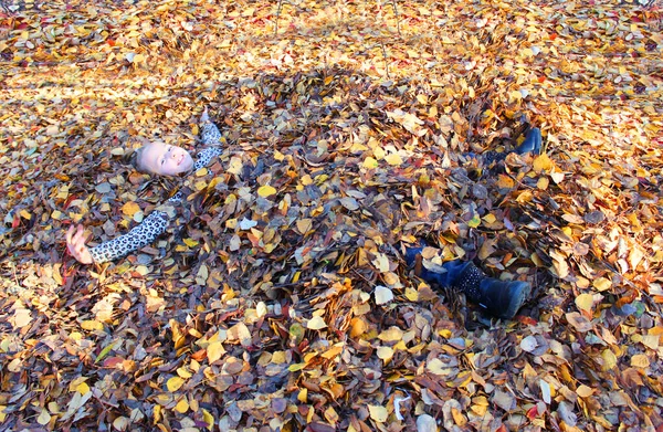 Meisje dat speelt met herfstbladeren. verstrooit bladeren in het park en lacht — Stockfoto