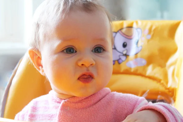 Baby Um close-up bonito loirinha de 1 ano de idade contra um fundo verde turvo. Seus grandes olhos azuis estão olhando para a câmera. — Fotografia de Stock