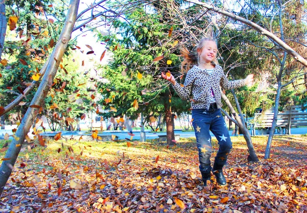 Meisje dat speelt met herfstbladeren. verstrooit bladeren in het park en lacht — Stockfoto
