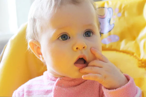 Baby Um close-up bonito loirinha de 1 ano de idade contra um fundo verde turvo. Seus grandes olhos azuis estão olhando para a câmera. — Fotografia de Stock