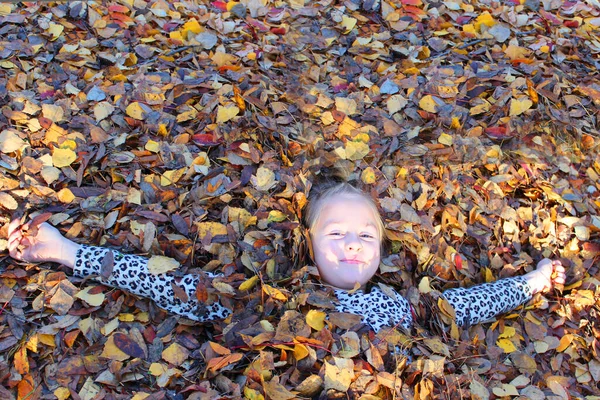 Menina brincando com folhas de outono. dispersa folhas no parque e ri — Fotografia de Stock