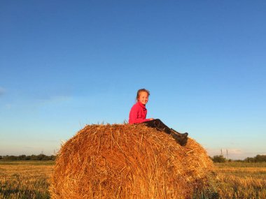 Kırsal, sarı saçlı, samanlıkta sırıtan kırmızı kazaklı, lastik çizmeli, hasattan sonra sarı buğday tarlalı tatlı bir kız. Samanlık arazilerinde, mavi gökyüzünde. Bir çocuk koşar