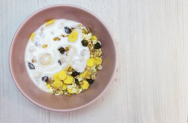 Pembe tabakta müsli, üst manzara. Müsli, taze süt, yoğurt ya da kefir. Müsli yulaf ezmesinden, kurutulmuş meyve, fındık ve ayçiçeği tohumlarının karışımından yapılır. Beyaz üzerine.