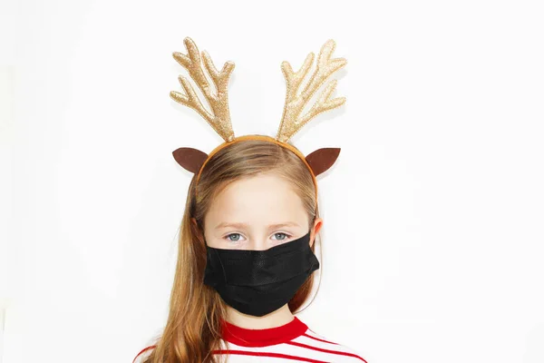 Karantinaya alınmış Noel Baba geyiği, güzel kız kırmızı kazağı ve yeni yıl hediyesi. Noel Baba şapkalı mutlu küçük kızın bir Noel 'i var. Beyaz arka plan pankartıyla siyah bir maskeyle, Noel 'de