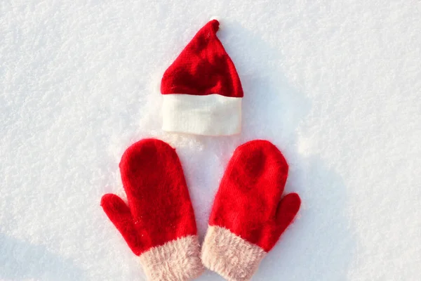 Red Santa hat and knitted mittens lie on the snow. mitten lying on the snow in winter. Holiday Decorations Christmas and New Year Traditions Panoramic Banner Free Space Text Top View Flst lay — Stock Photo, Image