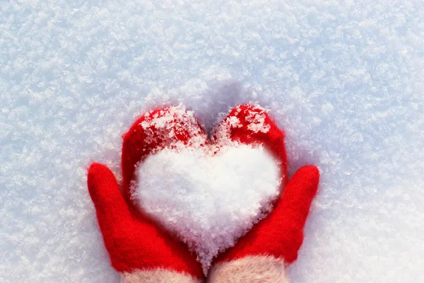 Hands in knitted mittens with a heart made of snow on a winter day. ... Snowy heart in hands. Human hands in warm red mittens with a snowy heart on a background of snow. Love winter christmas or Royalty Free Stock Photos