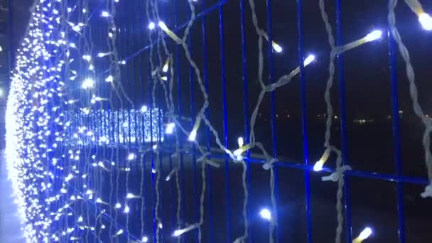 Nochebuena, día de invierno con nevadas. guirnaldas en la valla y una vista de las luces de la ciudad, luz de la linterna, copos de nieve volando. en el suelo, brillantes nevadas de invierno, hermosa iluminación artística — Vídeos de Stock