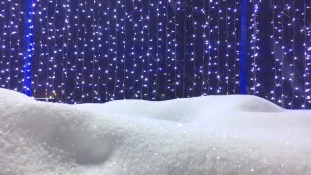 Nochebuena, día de invierno con nevadas. guirnaldas en la valla y una vista de las luces de la ciudad, luz de la linterna, copos de nieve volando. en el suelo, brillantes nevadas de invierno, hermosa iluminación artística — Vídeos de Stock