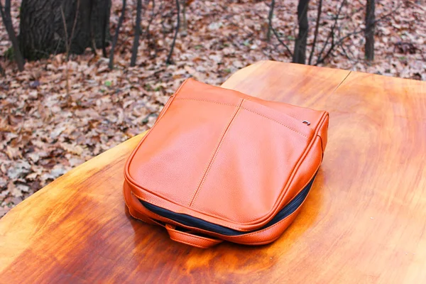 Brown Backpack Genuine Leather Backpack. or backpack on a wooden table in the autumn forest. Modern leather backpack left view, Leather backpack with thin straps on a wooden background. light brown