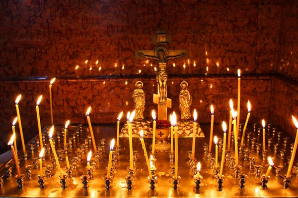 Lit kostelní svíčky ve zlaceném svícnu v chrámu ve tmě. Žlutý vosk zapálené svíčky stojí v kostele, záře. Voskové svíčky na podlaze svícnu v křesťanském kostele. Rituální svíčky, svaté — Stock fotografie