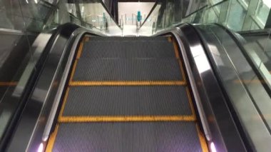 Modern lüks yürüyen merdivenler. Hareket eden kazıcı adımlarının videosu değişiyor. Bir alışveriş merkezindeki merdiven kazıcıyla plastik parmaklıklı neon ışıklı, merdiven manzaralı, zemine inen.