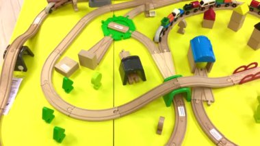 Bir çocuk ahşap bir trenle oynar ve evde bir oyuncak tren yolu inşa eder, bir anaokulunda ya da bir alışveriş merkezinde. Parlak sarı arka plan. Anaokulu ve anaokulu çocukları için eğitici oyuncaklar. İç mekan
