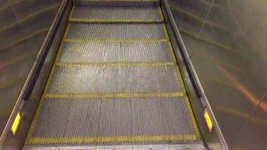 Modern lüks yürüyen merdivenler. Hareket eden kazıcı adımlarının videosu değişiyor. Bir alışveriş merkezindeki merdiven kazıcıyla plastik parmaklıklı neon ışıklı, merdiven manzaralı, zemine inen.