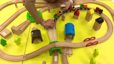 Bir çocuk ahşap bir trenle oynar ve evde bir oyuncak tren yolu inşa eder, bir anaokulunda ya da bir alışveriş merkezinde. Parlak sarı arka plan. Anaokulu ve anaokulu çocukları için eğitici oyuncaklar. İç mekan