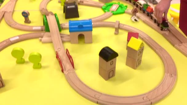 Dziecko bawi się drewnianym pociągiem i buduje koleje zabawkowe w domu, w przedszkolu lub w centrum handlowym. Jasnożółte tło. Zabawki edukacyjne dla dzieci przedszkolnych i przedszkolnych. wewnątrz — Wideo stockowe