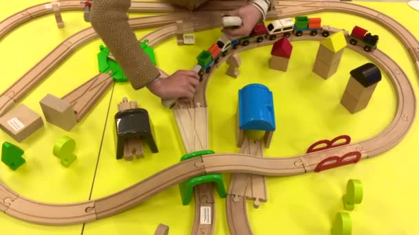 A child plays with a wooden train and builds a toy railroad at home, in a kindergarten or in a shopping mall. Bright yellow background. Educational toys for preschool and kindergarten children. indoor — Stock Video