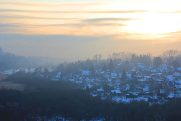 Piękny widok na wypełnienie mgły zimowy poranek na krajobraz domów. Krajobrazy widok z góry o zachodzie słońca w miejscowości. Kominy dymne na dachach ze śniegiem wydzielają dym, smogi o wschodzie słońca — Zdjęcie stockowe