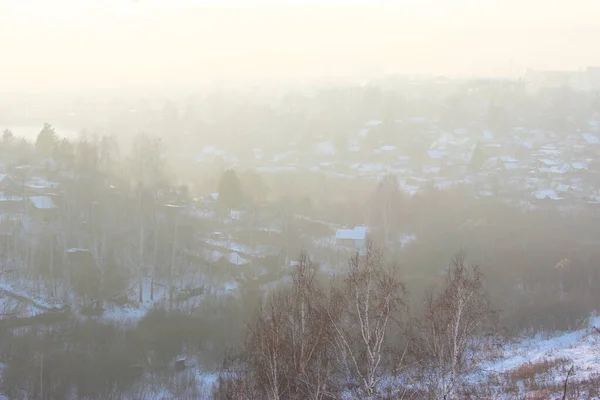 Piękny widok na wypełnienie mgły zimowy poranek na krajobraz domów. Krajobrazy widok z góry o zachodzie słońca w miejscowości. Kominy dymne na dachach ze śniegiem wydzielają dym, smogi o wschodzie słońca — Zdjęcie stockowe