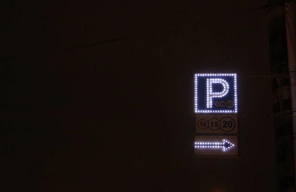 Parcheggio segno luce al neon di notte sopra freccia cielo scuro illuminato da lanterne. strada di notte in inverno — Foto Stock