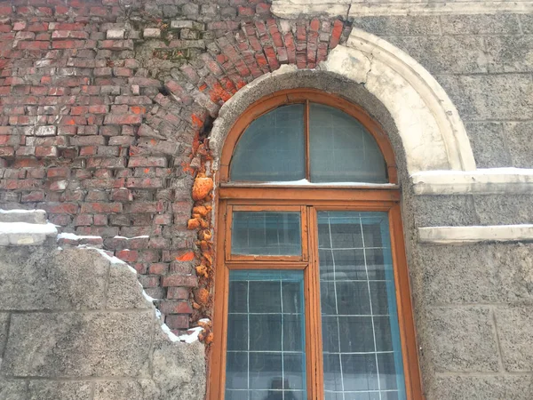 Antigua casa en ruinas en la ciudad, gran ventana antigua, ventanas sucias, decoración colapsada, yeso de ladrillo viejo visible, metal oxidado. Un edificio gris sombrío en el centro de la ciudad necesita renovación y —  Fotos de Stock