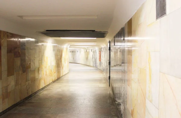 Un largo túnel vacío conduce a la distancia. Cruce peatonal en el metro de una estación a otra, las paredes están hechas de mármol claro. Túnel del metro sin gente. Transporte público —  Fotos de Stock