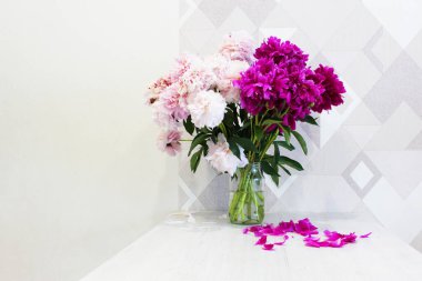 Ahşap bir masada pembe ve beyaz şakayık demeti, şeffaf cam bir vazoda kırmızı şakayık demeti, renkli bir buket. Konforlu ev konsepti. dikey görüntü. için yer