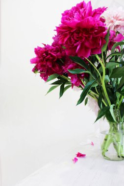 Ahşap bir masada pembe ve beyaz şakayık demeti, şeffaf cam bir vazoda kırmızı şakayık demeti, renkli bir buket. Konforlu ev konsepti. dikey görüntü. için yer