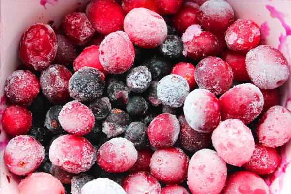 Frozen fruits of currants, cranberries, lingonberries in ice crystals. Background mix of frozen berries. Design concept. Copy space. Selective focus. Close frozen cranberries in pink bowl. Selective — Stock Photo, Image