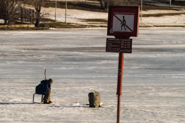 Le pêcheur en pêche hivernale et une pancarte interdisant l'accès à la glace — Photo