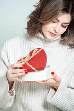 Güzel kız, kırmızı kalp hediye kutusunu aç. Sevgililer Günü. Doğum günün kutlu olsun. Kız evde bir hediye alıyor..