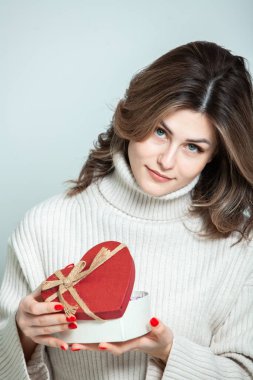 Güzel kız, kırmızı kalp hediye kutusunu aç. Sevgililer Günü. Doğum günün kutlu olsun. Kız evde bir hediye alıyor..