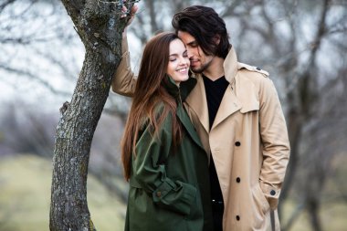 Genç ve şık bir çiftin güzel şehvetli portresi. Parkta yağmurluk giymiş güzel esmer bir çiftin resmi. Mutlu aile