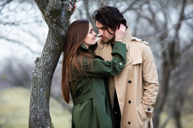 Genç ve şık bir çiftin güzel şehvetli portresi. Parkta yağmurluk giymiş güzel esmer bir çiftin resmi. Mutlu aile