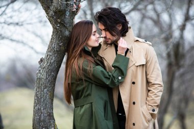 Genç ve şık bir çiftin güzel şehvetli portresi. Parkta yağmurluk giymiş güzel esmer bir çiftin resmi. Mutlu aile