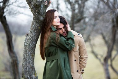 Genç ve şık bir çiftin güzel şehvetli portresi. Parkta yağmurluk giymiş güzel esmer bir çiftin resmi. Mutlu aile